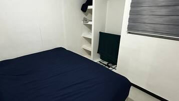 A bedroom with a bed, a wardrobe, and a window with blinds.