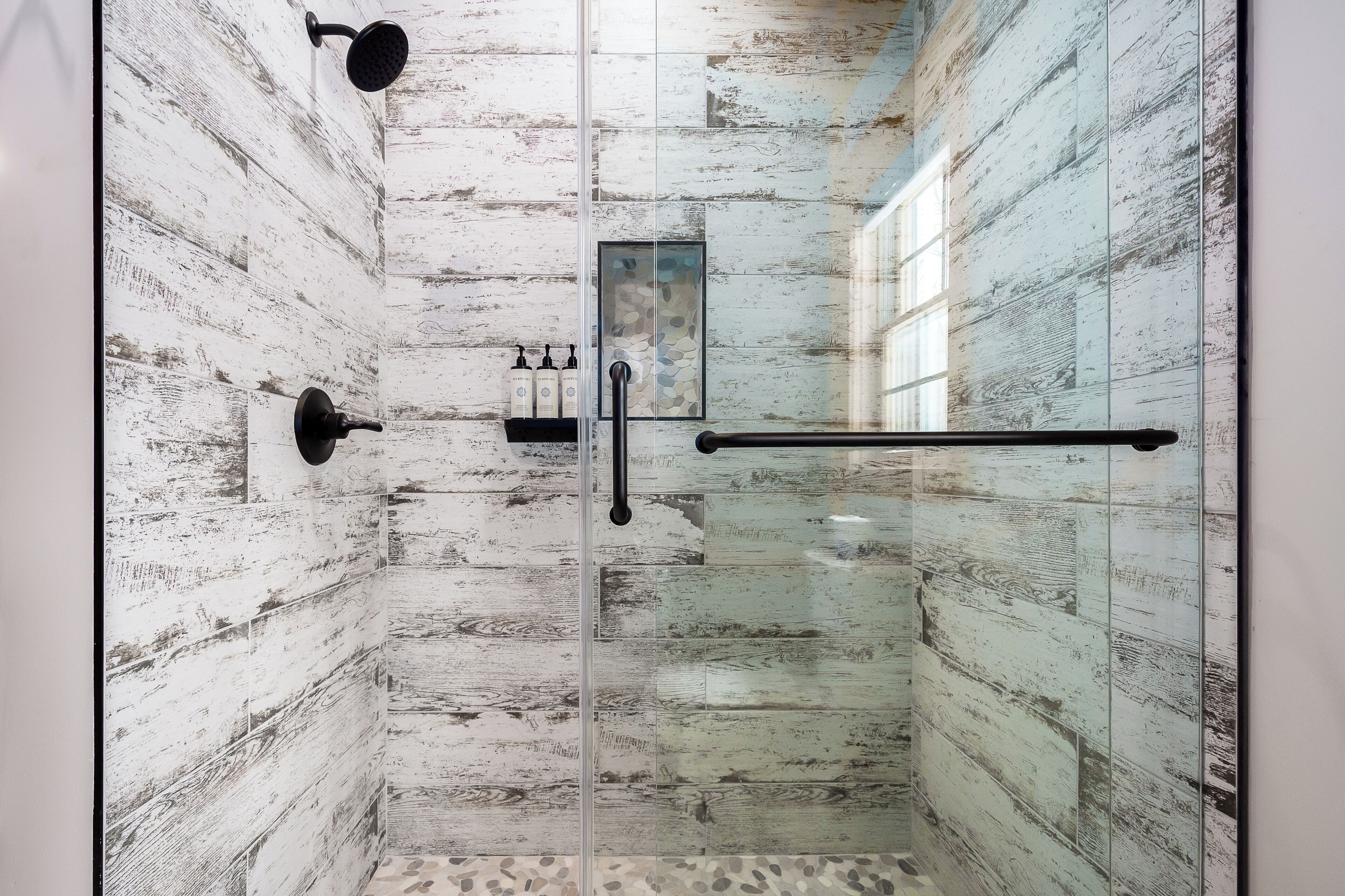 A glass-enclosed shower with a rustic wall design, a handheld showerhead, and a glass door.