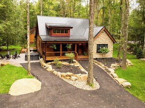 A cabin with a deck, a stone building, and a forested backdrop. - Willowcrest: Brand NEW, Lake Access, Dog Friendly, Hot Tub (Oakland)