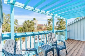 A covered outdoor area with blue railings, two Adirondack chairs, and a view of a pool and buildings in the background. - Southern Harbor Retreat | Heated Pool, Game Room & Easy Walk to the Beach (Indian Rocks Beach)