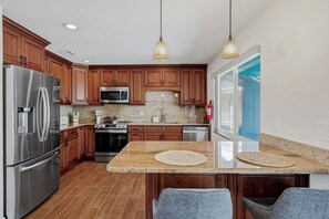 A kitchen with wooden cabinets, stainless steel appliances, granite countertops, and pendant lighting. - Southern Harbor Retreat | Heated Pool, Game Room & Easy Walk to the Beach (Indian Rocks Beach)