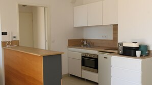 Une cuisine compacte dotée d’un plan de travail en bois, d’un four encastré, d’un lave-vaisselle et de meubles de rangement blancs.