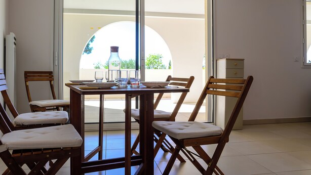 Un coin repas avec une table dressée pour quatre personnes, des chaises et une vue à travers une porte vitrée.