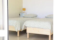 Une chambre avec deux lits en bois, une petite table de chevet avec une lampe et un mur sobre.