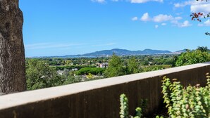 Une vue depuis un balcon donnant sur un paysage composé d’arbres, d’un ciel dégagé et de montagnes lointaines.