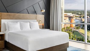 Una habitación de hotel moderna con una cama grande, una mesita de noche de madera y vistas a la ciudad.