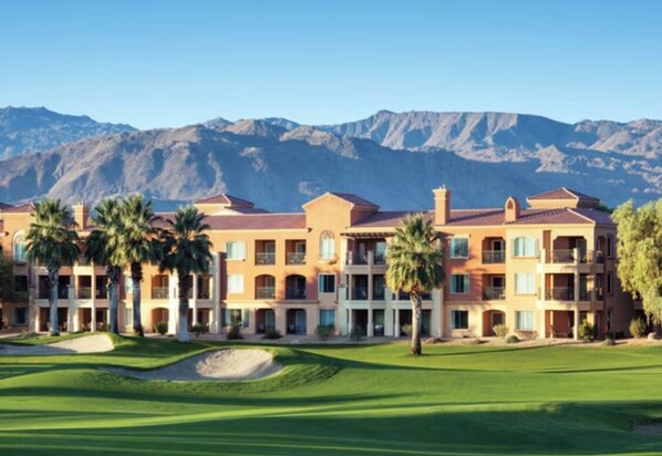 Un hôtel à plusieurs étages, doté d’un terrain de golf à l’avant et entouré de montagnes.