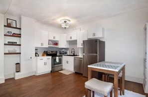 A modern kitchen with white cabinets, stainless steel appliances, and a wooden dining table.