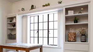 A dining area with a wooden table and chairs, a window with grid blinds, and white shelving with various items. - Prime football location- condo walking distance from stadium (Knoxville)