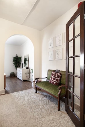 A living room with a green sofa, a patterned rug, a white dresser, and framed artwork on the wall.