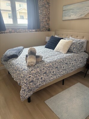 A bedroom with a bed, a stone wall, a window, and a painting on the wall. - NEW 2 bedroom, (queens)  1 bathroom VRBO, comfy & serene. “ASPEN’s Suite Escape” (Saskatoon)