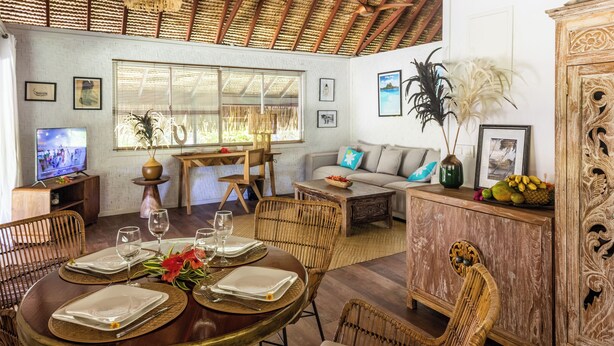 Uma sala de jantar com uma mesa redonda posta para quatro pessoas, rodeada por cadeiras de vime.