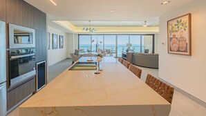 A modern kitchen with a large island, dining area with chairs, and a view of the sea. - Sonoran Star 1-0805-3Bed (Puerto Peñasco)