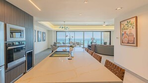 Eine moderne Küche mit einer großen Kochinsel, einem Essbereich mit Stühlen und Blick aufs Meer.