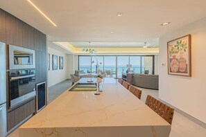 Eine moderne Küche mit einer großen Kochinsel, einem Essbereich mit Stühlen und Blick aufs Meer.