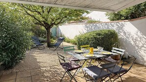 Eine Terrasse mit Tisch für vier Personen, umgeben von Stühlen und einem kleinen Baum.