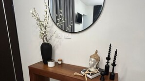 Een moderne console tafel met een ronde spiegel, een vaas met takken, een klein krukje en decoratieve objecten.