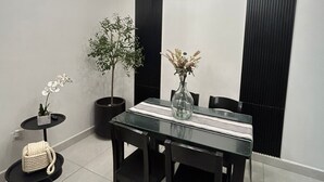 Een eetruimte met een glazen tafel, zwarte stoelen, een zwart plafondlamp en potplanten.