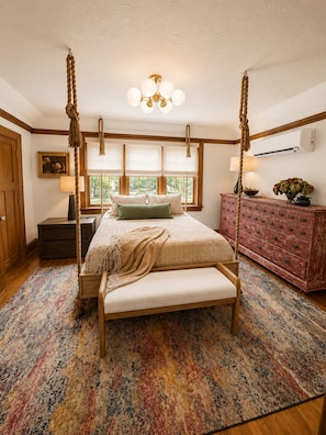 A four-poster bed with a canopy, a wooden bench, a patterned rug, a dresser, and a picture on the wall.