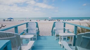 A beach view with a wooden deck leading to white chairs and tables. - Happy Ours – NEW LISTING, Direct Beachfront Home On Magnolia (Anna Maria)