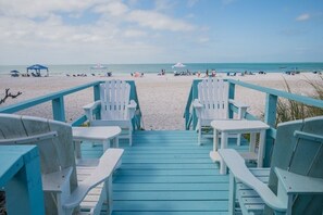 A beach view with a wooden deck leading to white chairs and tables. - Happy Ours – NEW LISTING, Direct Beachfront Home On Magnolia (Anna Maria)