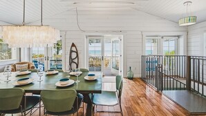A dining area with a table set for four, a hanging light fixture, and a view of the ocean through large windows. - Happy Ours – NEW LISTING, Direct Beachfront Home On Magnolia (Anna Maria)