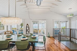 Un coin repas avec une table dressée pour quatre personnes, un luminaire suspendu et une vue sur l’océan grâce à de grandes fenêtres.
