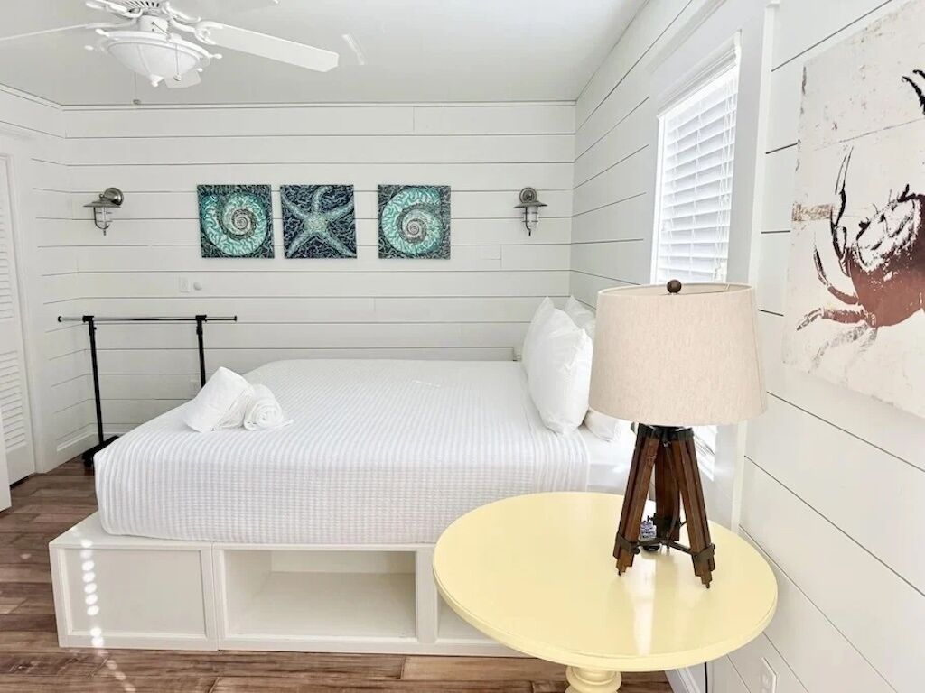 A bedroom with a bed, a bedside table with a lamp, and wall art.