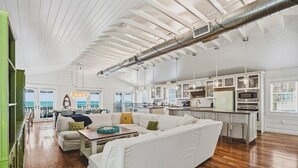 A spacious living area with a white sofa, a dining table, and a kitchen area with modern appliances. - Happy Ours – NEW LISTING, Direct Beachfront Home On Magnolia (Anna Maria)