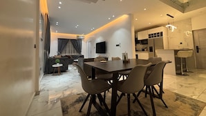 A modern living room with a dining area, kitchen, and a staircase.