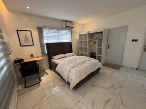 A bedroom with a bed, a desk, a wardrobe, and a wall-mounted air conditioner.