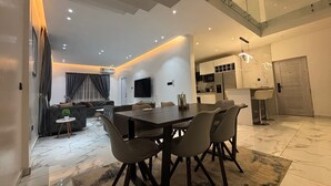A modern living room with a dining area, a kitchen, and a staircase.