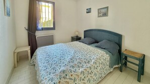 Et soveværelse med seng, et natbord, et vindue med gardiner, en radiator og to billeder hængt på væggen.