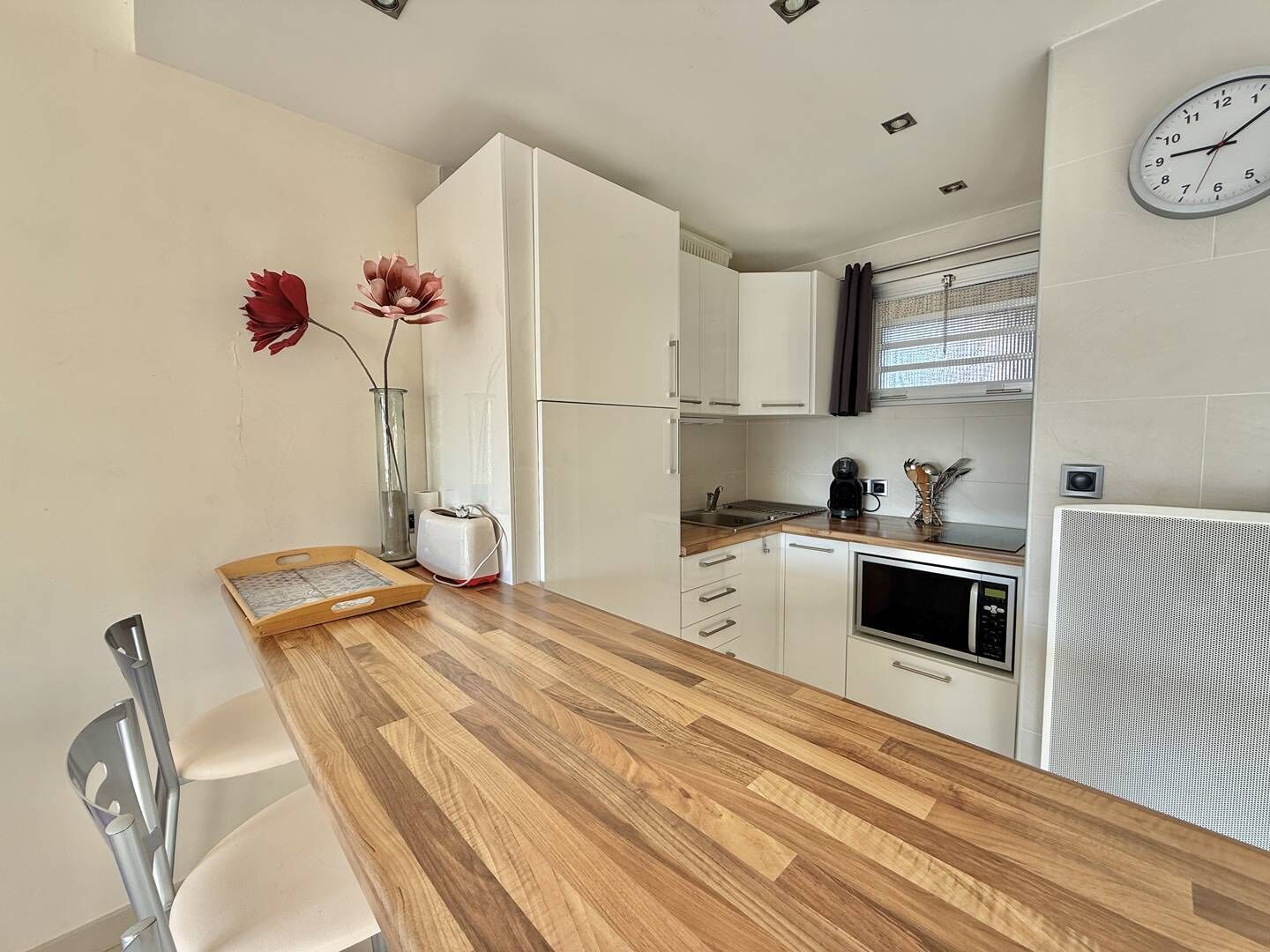 A modern kitchen with white cabinets, a wooden countertop, a toaster, a kettle, and a clock on the wall.