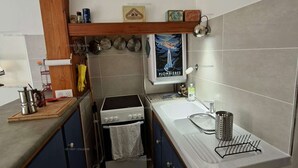 Una cocina compacta con estufa, horno, lavabo y un pequeño estante con utensilios de cocina.