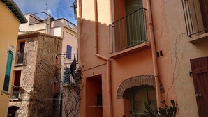 Una calle estrecha con edificios que tienen balcones, un muro de piedra y un pequeño jardín.