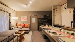 A compact living space with a sofa, a dining table set for four, a kitchen area, and a door leading to another room.