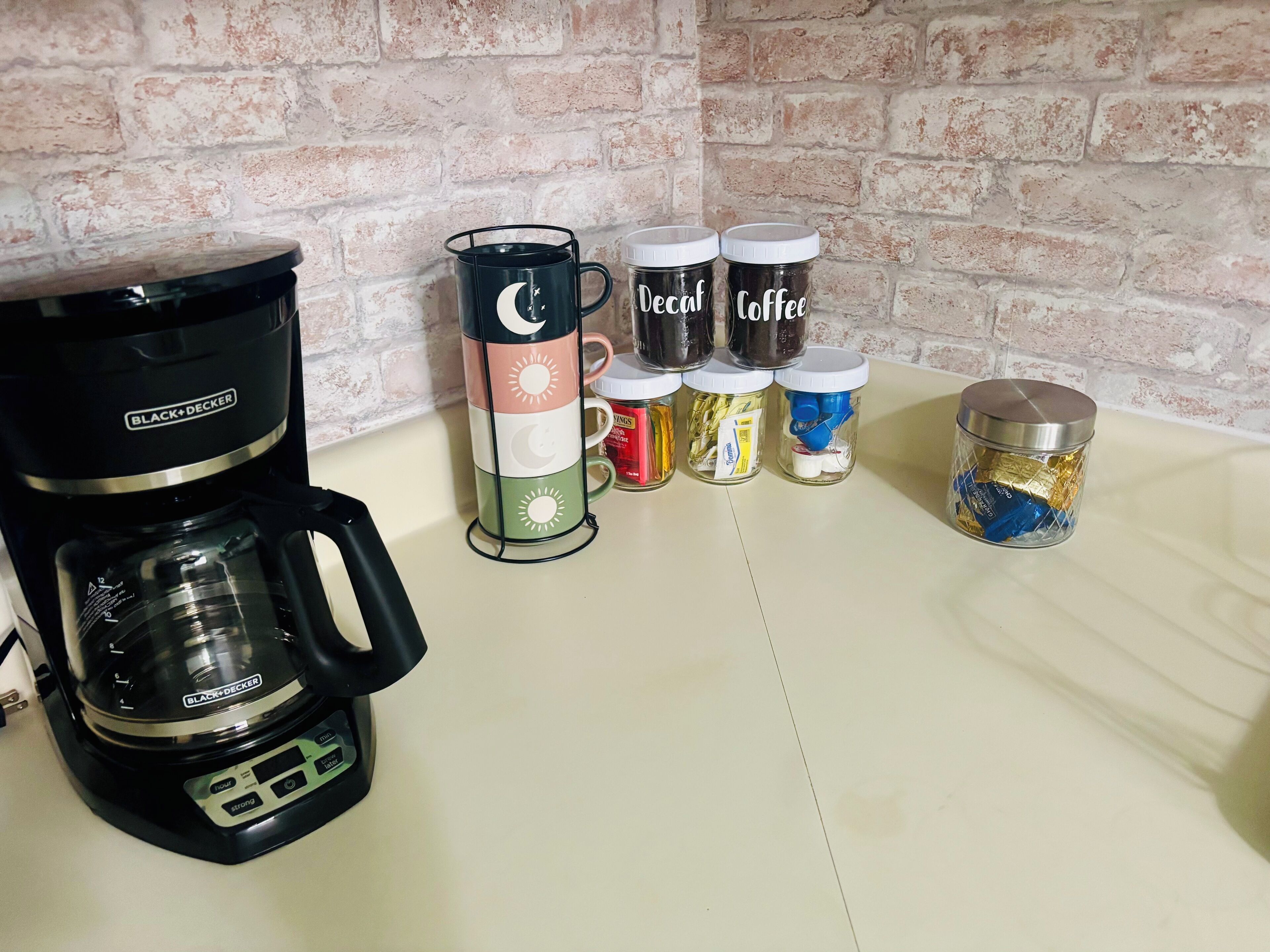 Une machine à café, une tasse ornée de motifs représentant la lune et le soleil, et plusieurs bocaux contenant divers articles liés au café, le tout posé sur un plan de travail.