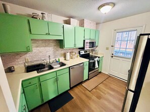 A kitchen with green cabinets, a microwave, a dishwasher, and a refrigerator. - Walk to Shoppes of Kildaire & Close to Bond Park! (Cary)