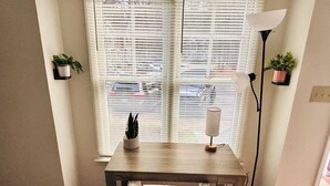 Une pièce avec une fenêtre, une table, une chaise, une lampe et deux plantes en pot.