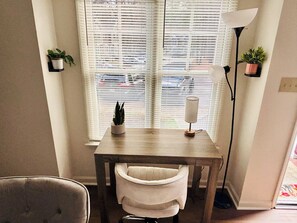 A room with a window, a table, a chair, a lamp, and two potted plants. - Walk to Shoppes of Kildaire & Close to Bond Park! (Cary)