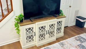 Un téléviseur posé sur un meuble en bois doté de portes en verre décoratives, une plante en pot et une poubelle.