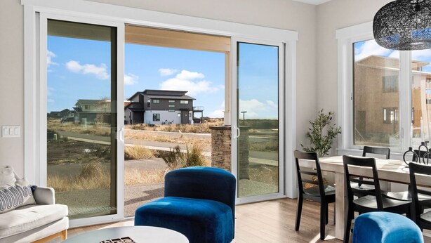 A modern living room with a sofa, a blue armchair, a dining table with chairs, and a large sliding glass door leading to an outdoor area. - Oceanview Retreat - Hot Tub + Game Garage + Spa Suite + Kids Cave - Westport, WA (Westport)