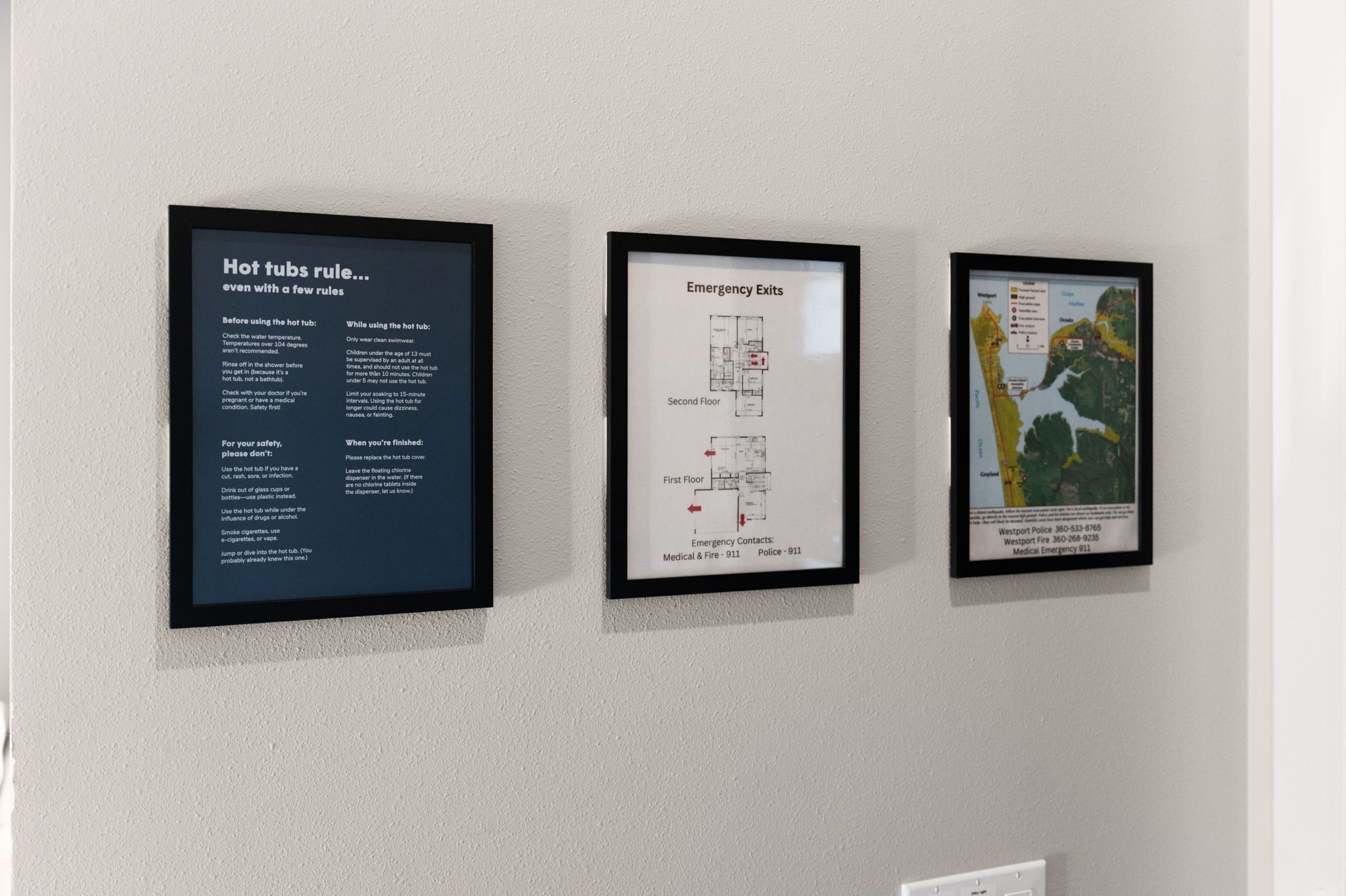 Three framed informational posters on a wall: one about hot tub safety rules, one showing emergency exits on the second floor, and one with a map of the area.