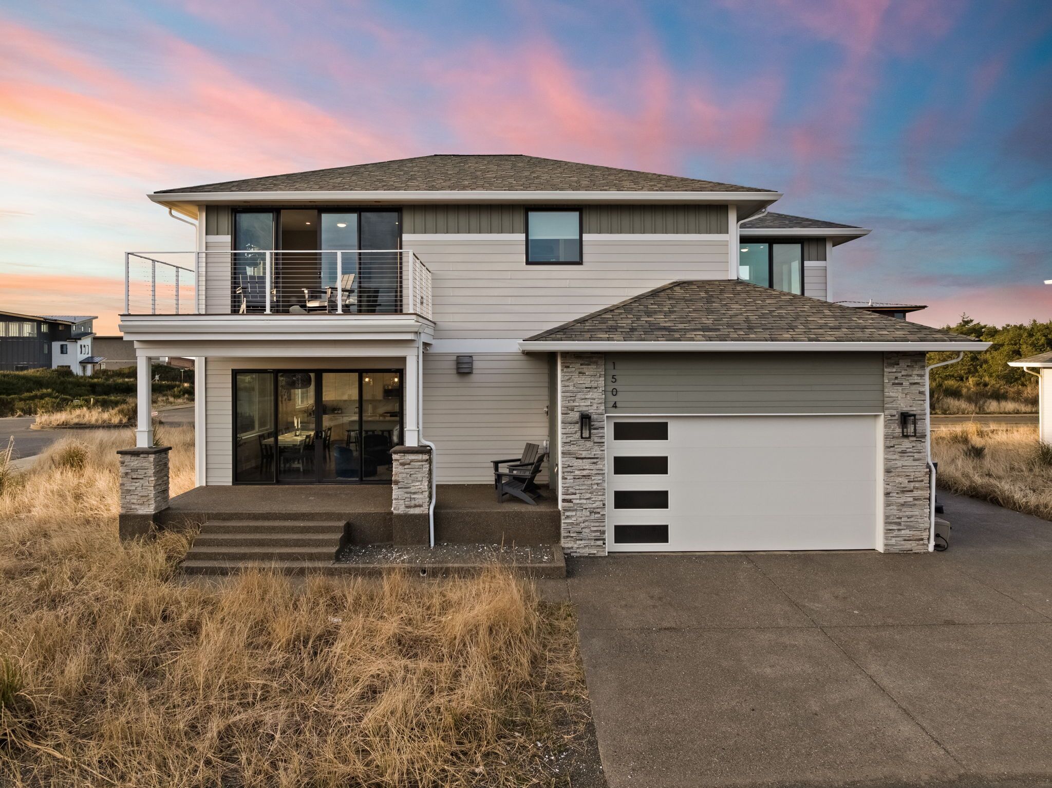 Une maison moderne à deux étages, dotée d’un balcon, d’un garage et d’un mur d’accent en pierre.