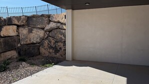 A concrete patio area with a stone wall and a metal fence. - Cozy Casita with Mountain Views (Cedar City)