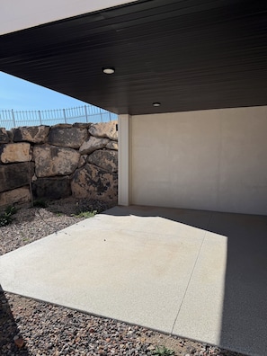 A concrete patio area with a stone wall and a metal fence.