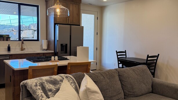 A modern kitchen with a central island, wooden cabinets, and a dining area with a table and chairs. - Cozy Casita with Mountain Views (Cedar City)