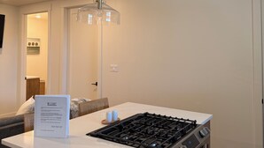 A modern kitchen with a gas stove, wooden cabinets, a white countertop, and a hanging light fixture. - Cozy Casita with Mountain Views (Cedar City)