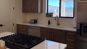 A modern kitchen with a gas stove, a built-in dishwasher, wooden cabinets, a window with a view, and a stainless steel refrigerator. - Cozy Casita with Mountain Views (Cedar City)